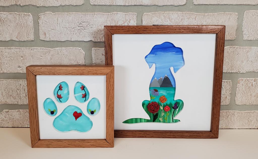 small blue paw print with embroidered flower details. A larger dog silhouette with a mountain scene background and embroidered flower details.
