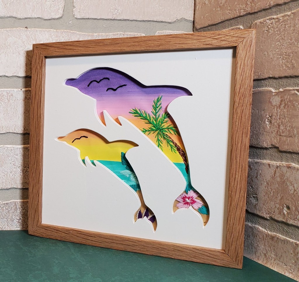 Large and small dolphins silhouette with a sunset and beach background with embroidered palm tree and flower details.