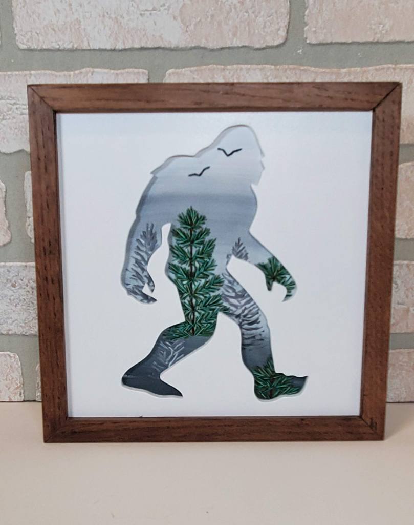Bigfoot silhouette with hazy sky background and embroidered tree designs