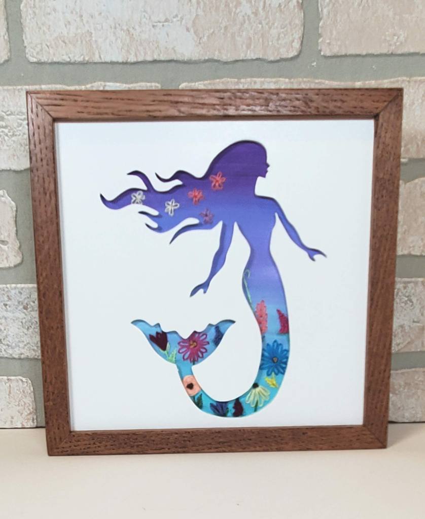 Mermaid side view silhouette with purple and blue background with embroidered flower details.