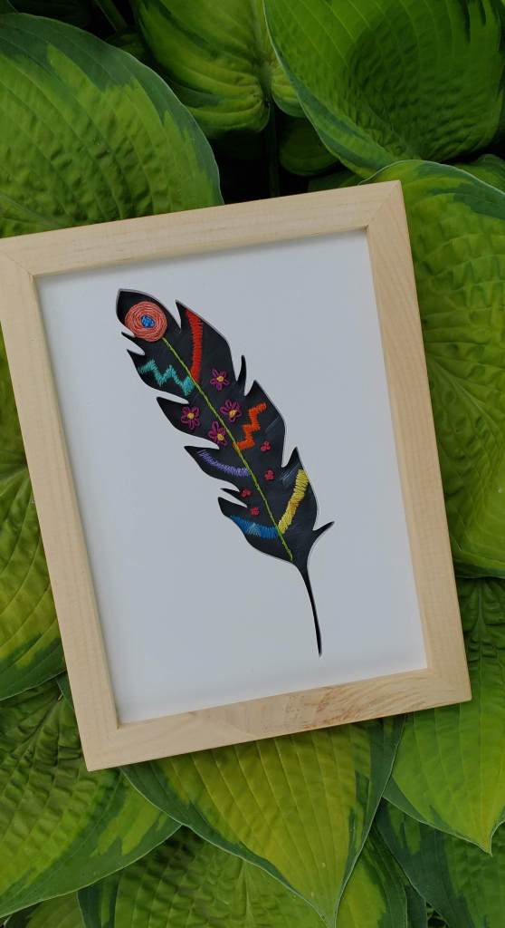 Single feather silhouette with black background and embroidered geometric patter inside.