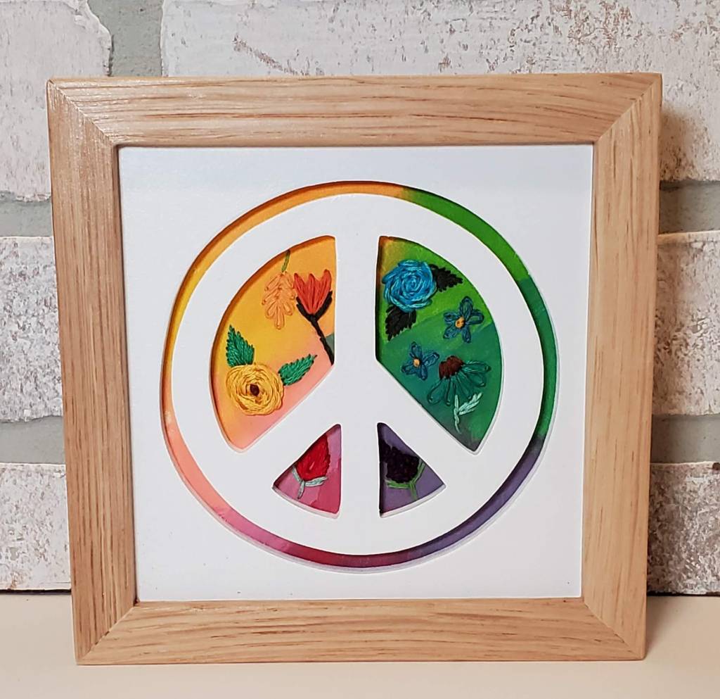 Peace sign silhouette with rainbow color background with embroidered flower details.