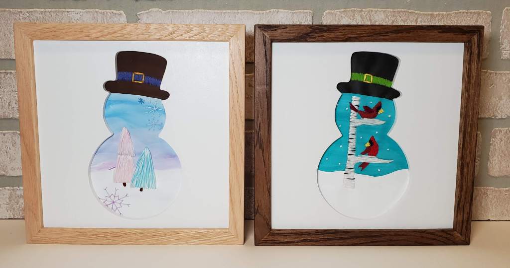 Two snowman silhouettes. One has embroidered tree design and one has embroidered cardinals sitting on a birch branch.