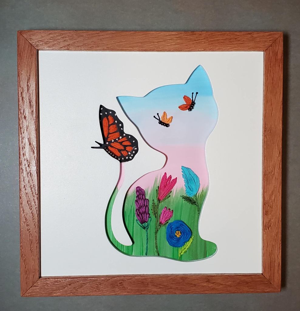 Cat side view silhouette with an orange butterfly sitting on its tail. Pastel sky background with embroidered flower details.