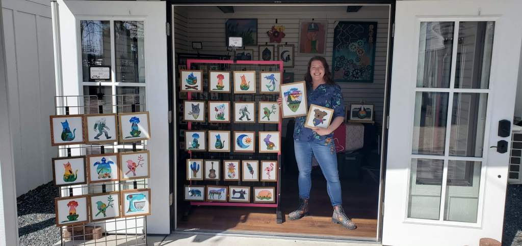 woman standing next to a rack display of embroidery silhouette artwork.