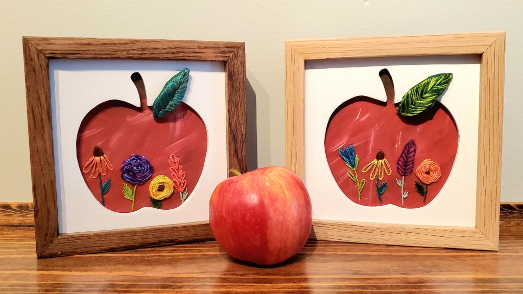 Two apple silhouettes with red backgrounds and embroidery floral designs.